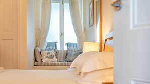 A hotel room with a bed, a window with curtains, a sofa with cushions, and a lamp. - 3 Bed in Fowey (oc-o33078) (Fowey)