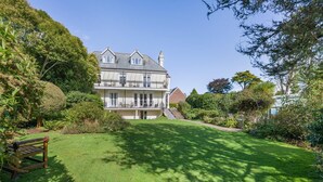 A two-story house with a well-maintained lawn and a wooden bench. - 3 Bed in Fowey (oc-o33078) (Fowey)