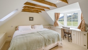 Un dormitorio con techo inclinado, una cama con colcha verde y blanca a rayas, una silla y una ventana con vista a un paisaje verde.