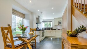 A modern kitchen with white cabinets, a dining area with a glass table, and a wooden staircase. - 1 Bed in Bodmin (oc-p00377) (Trevisquite Manor)