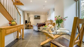 A modern dining area with a glass table, wooden chairs, and a view of the living room. - 1 Bed in Bodmin (oc-p00377) (Trevisquite Manor)