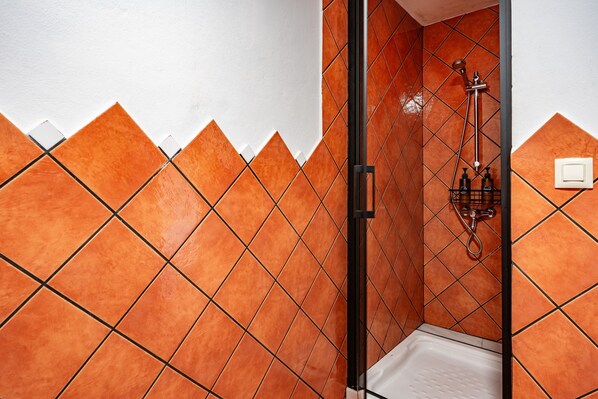 A bathroom with orange-tiled walls, a white bathtub, and a shower with a handheld showerhead.