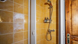 A bathroom with yellow tiles, a wooden door, and a shower with a handheld showerhead and a wall-mounted faucet.