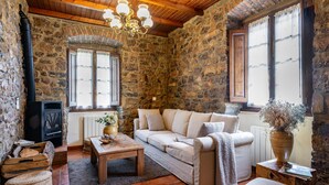 A stone-walled room with a sofa, a table, a fireplace, and a window. - Casa Rural Selmo in the Heart of Asturias (Zancornio)