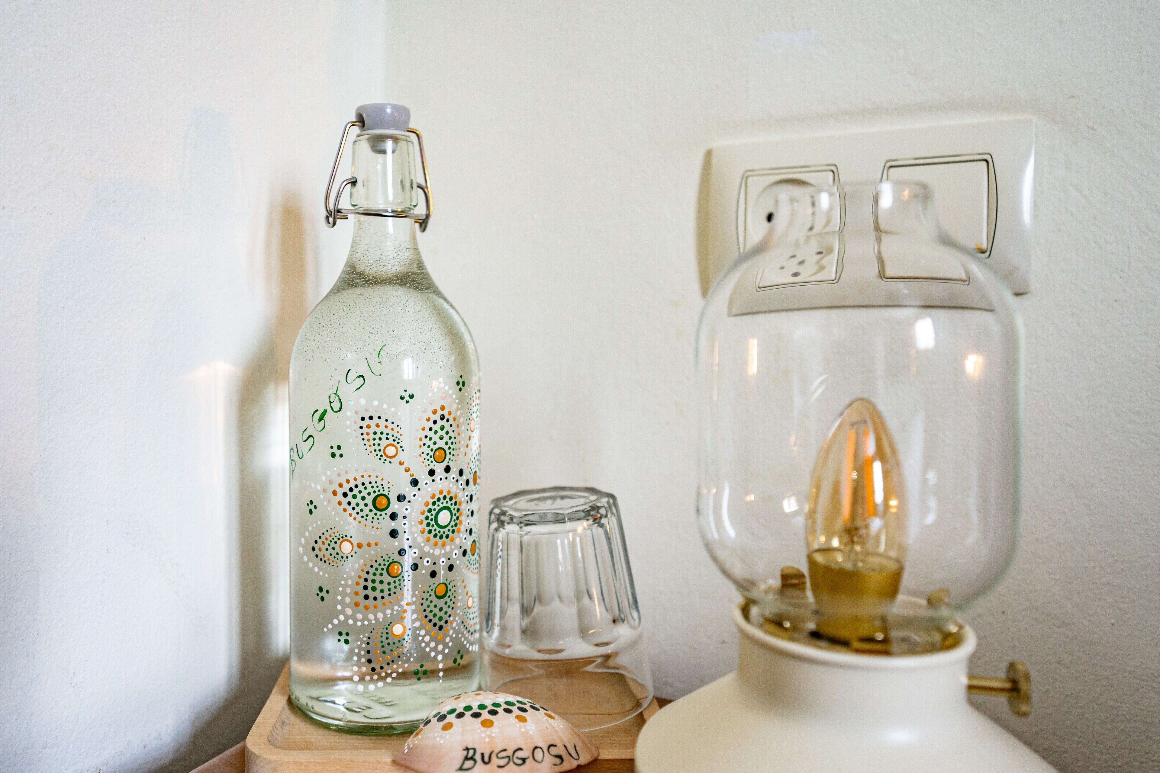 En klar glasflaske med metalspænde, et klart glas med en pære indeni, og et hvidt objekt med håndtag på en træoverflade.