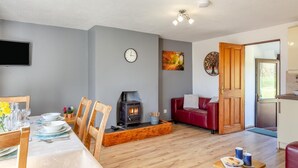 Un salon avec une cheminée, un coin repas avec une table dressée, un canapé rouge et un espace cuisine.