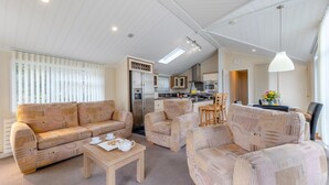 A modern living room with a sofa, armchairs, and a coffee table. A kitchen is visible in the background with a dining area. - 2 Bed in Tresaith (oc-c33408) (Tresaith)