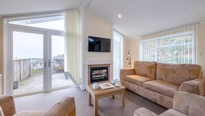 A spacious living room with a fireplace, a sofa set, a television mounted on the wall, and a large sliding glass door leading to an outdoor area. - 2 Bed in Tresaith (oc-c33408) (Tresaith)