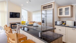 A modern kitchen with a central island, built-in appliances, and a dining area with wooden chairs. - 2 Bed in Tresaith (oc-c33408) (Tresaith)