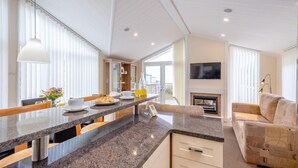 A modern kitchen with a granite countertop, a dining area with a table and chairs, a sofa, and a fireplace. - 2 Bed in Tresaith (oc-c33408) (Tresaith)