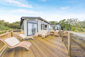 Une terrasse extérieure moderne, dotée de chaises longues et d’une table, et entourée de rampes en bois.