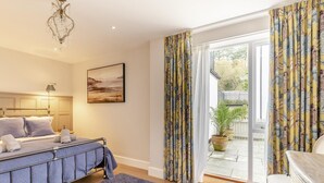 A bedroom with a bed, a chandelier, a painting, and a view of the outdoors through a sliding glass door. - 2 Bed in Fowey (oc-n33435) (Fowey)