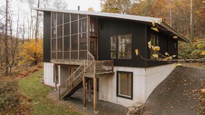 Une cabane moderne dotée d’une terrasse en bois et d’un escalier menant à un balcon.