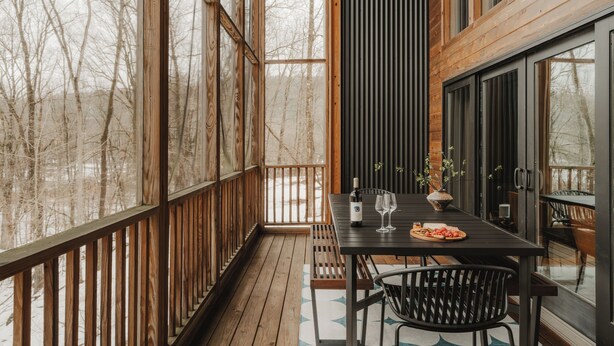 Une terrasse en bois avec une table et des chaises, une bouteille de vin et un verre posé sur la table.