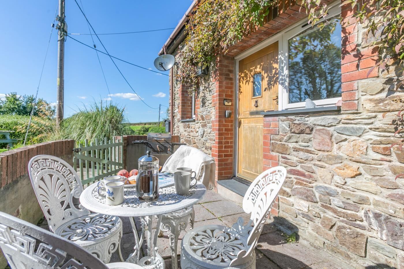Un bâtiment en pierre avec une porte en bois et un petit jardin agrémenté d’une table et de chaises.