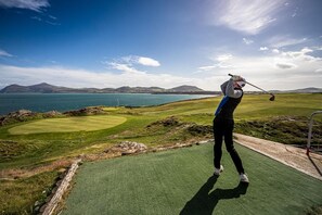 Ein Golfplatz mit Blick auf das Meer und Berge im Hintergrund.
