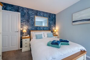 A bedroom with a bed, two bedside tables with lamps, a mirror, and a painting on the wall. - 4 Bed in Llanbedrog (oc-e33453) (Llanbedrog)