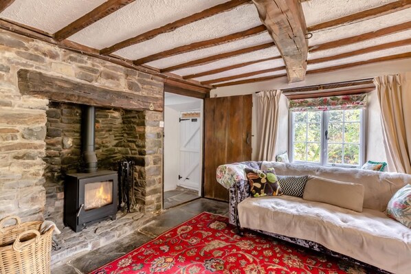 A cozy room with a stone fireplace, a sofa with floral cushions, and a red patterned rug.