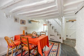 Zona de menjador amb taula preparada per a quatre, cadires de fusta, una catifa amb dibuixos i una escala que puja a un pis superior.
