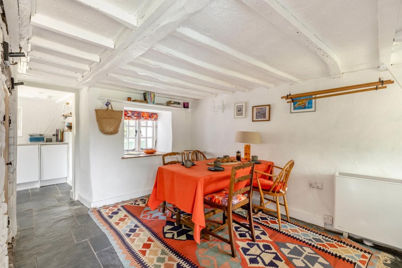 Zona pranzo con tavolo apparecchiato per quattro, una finestra con tenda colorata e una cucina sullo sfondo.