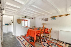 Een eetruimte met een tafel gedekt voor vier personen, een raam met een kleurrijk gordijn, en een keuken in de achtergrond.