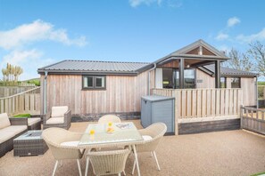 A wooden cabin with a patio area featuring wicker furniture and a glass table. - 2 Bed in Aberdaron (oc-o33727) (Aberdaron)