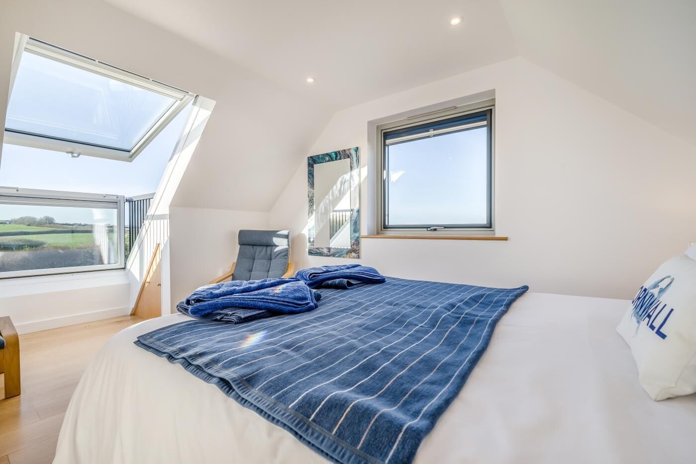 A bedroom with a large bed, two windows, a chair, and a view of the countryside.