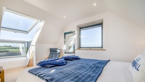 Een slaapkamer met een groot bed, twee ramen, een stoel en uitzicht op het platteland.
