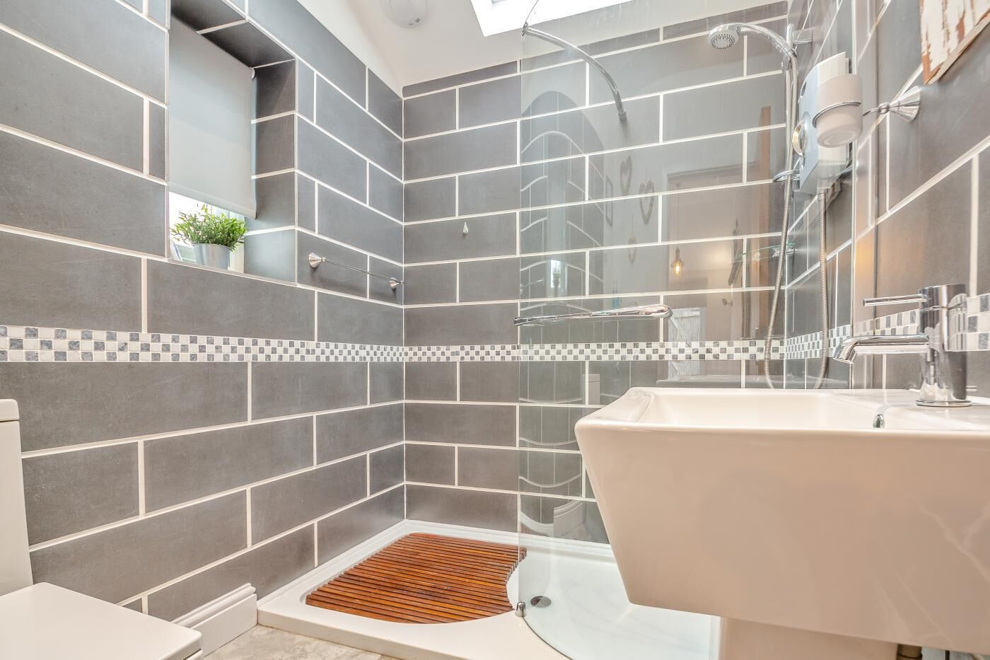 A modern bathroom with a shower, a sink, and a small window.