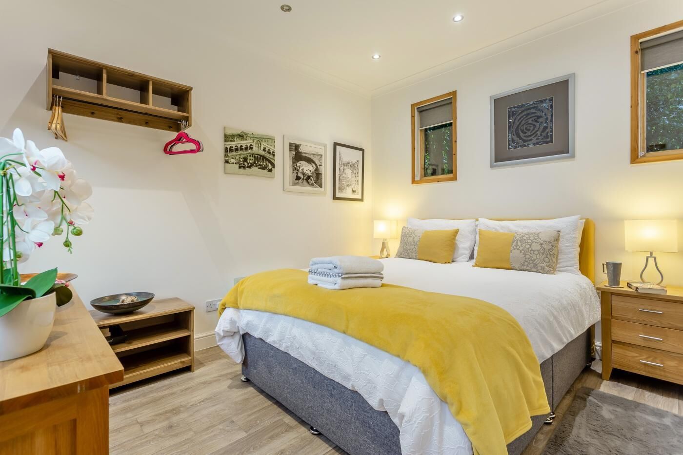 Ein modernes Schlafzimmer mit einem Bett, Nachttischen, einem Holzregal und Wandbildern.