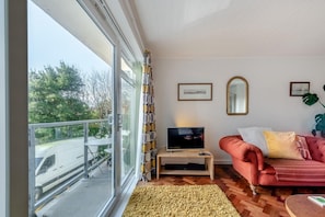 A living room with a TV, a red sofa, a large window, and a balcony.