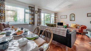A cozy living room with a dining area, large windows, a sofa, and a TV. - 2 Bed in Tenby (oc-t33804) (Tenby)