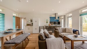 A modern living room with a sofa, a bench, a dining table, and a kitchen area with a bar. - 2 Bed in Harrowbarrow (oc-w33960) (Harrowbarrow)