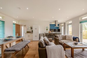 Ein modernes Wohnzimmer mit einer Couch, einer Bank, einem Esstisch und einer Küchenzeile mit Bar.