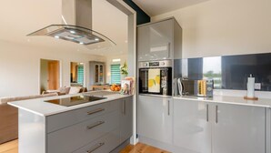 A modern kitchen with a central island, built-in oven, and a large window. - 2 Bed in Harrowbarrow (oc-w33960) (Harrowbarrow)