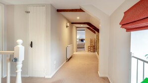 A narrow hallway with a white door on the left, a radiator, and a bed in the background. - 4 Bed in Shebbear (oc-a33728) (Shebbear)