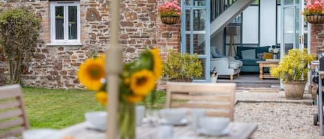 A stone building with a modern glass entrance, outdoor seating, and a table set for dining.