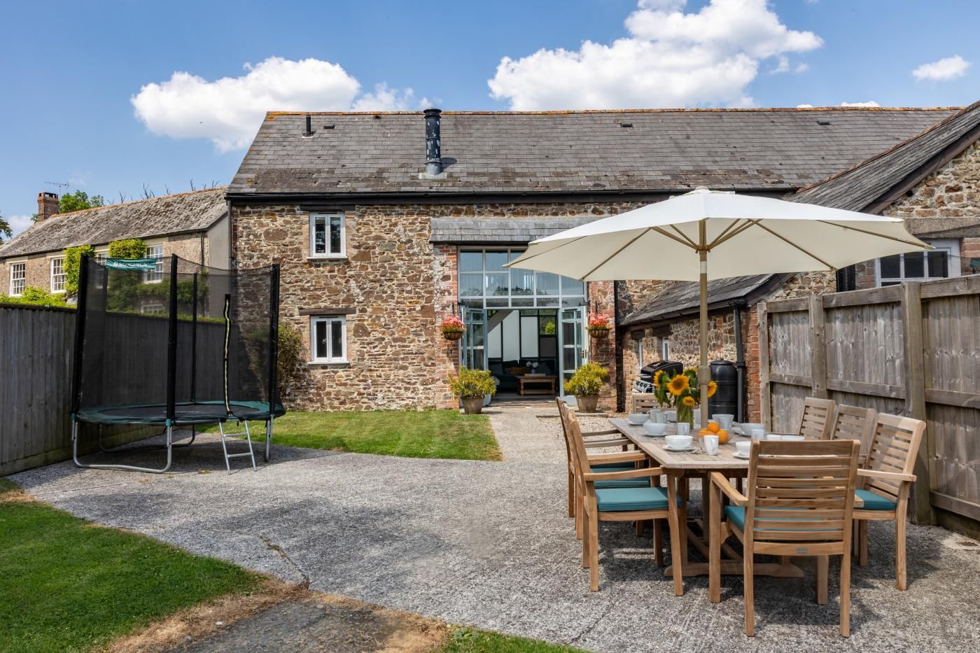 Una casa de piedra con un patio, un trampolín y una mesa con sillas y una sombrilla.