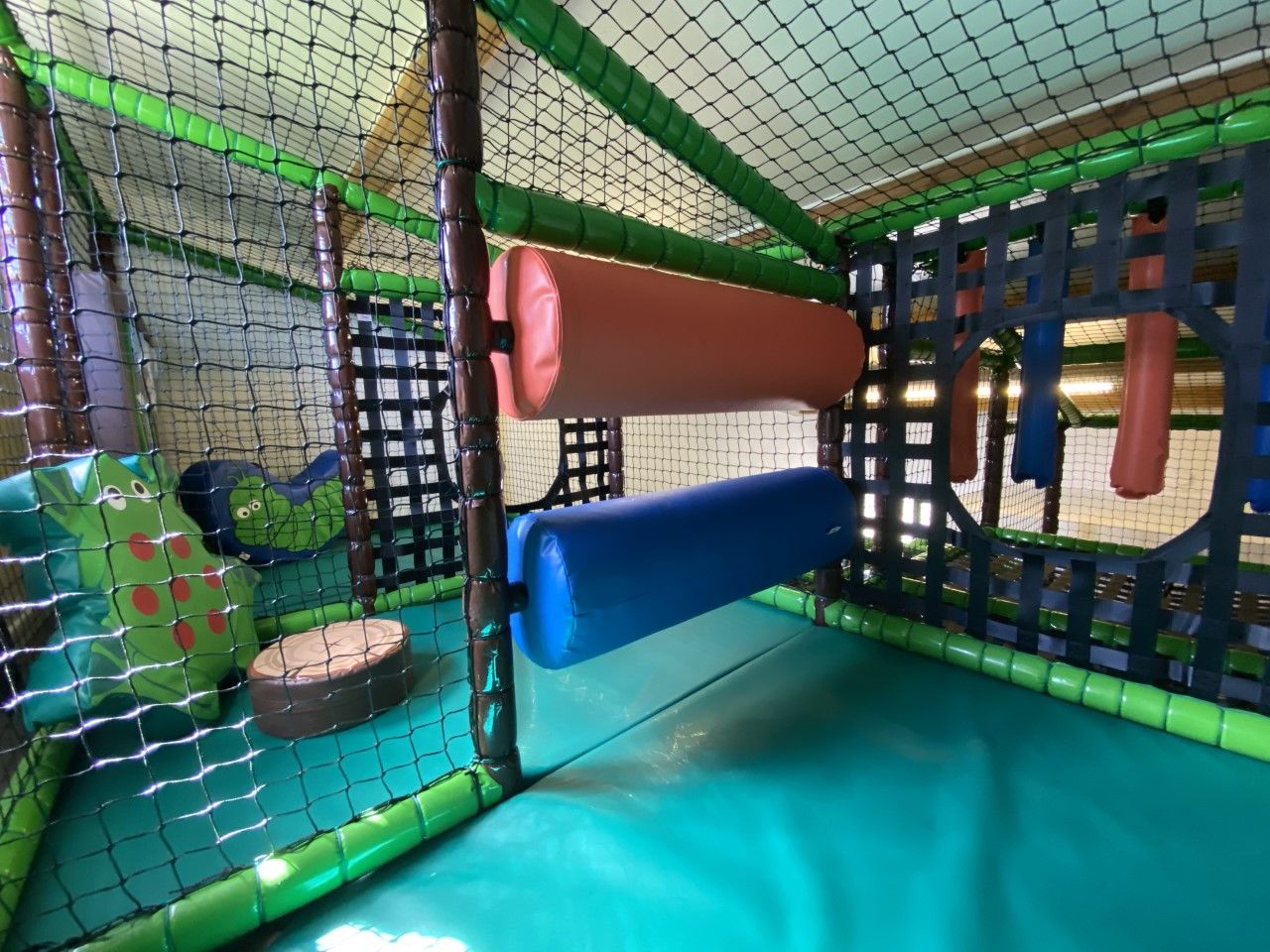 A play area with netted walls, padded structures, and soft flooring.