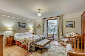 Une chambre à coucher comprenant un lit, deux tables de chevet, une chaise, un banc, une fenêtre avec des rideaux et un lustre.
