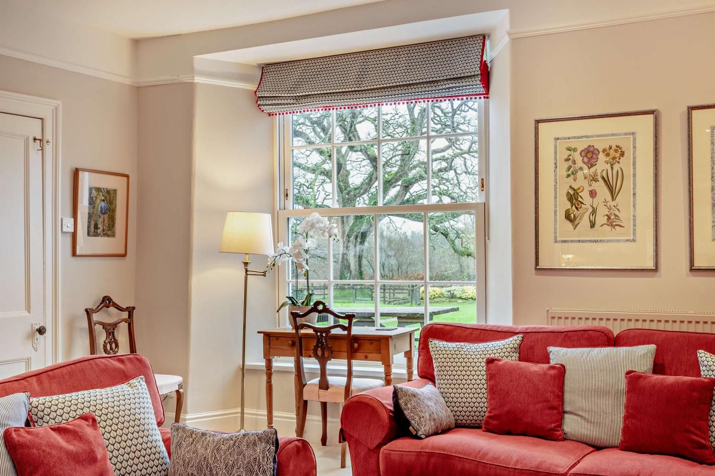 A cozy living room with a red sofa, a wooden table, and a window with a view of trees.