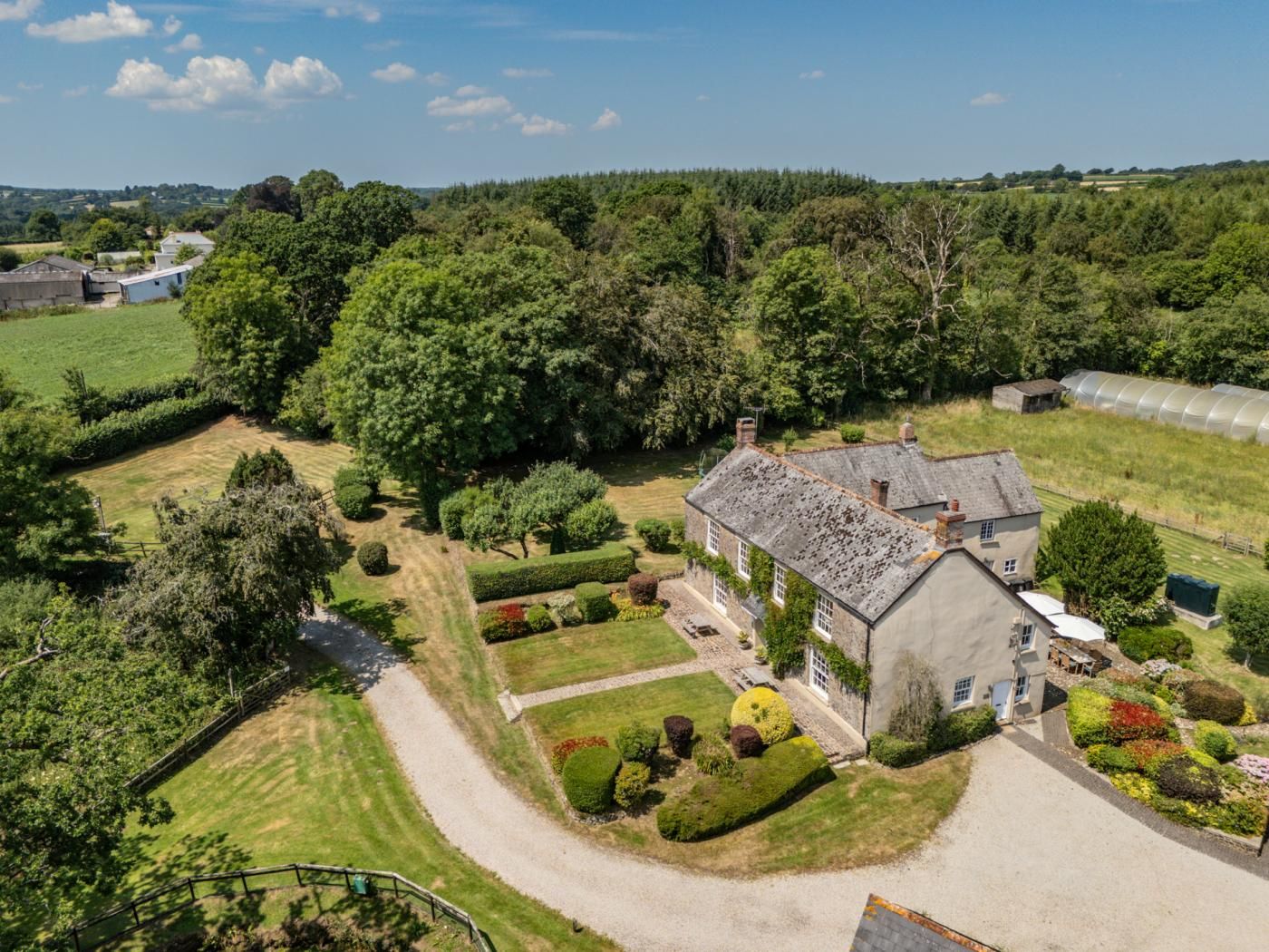 A large house with a well-maintained garden, a greenhouse, and a surrounding landscape.