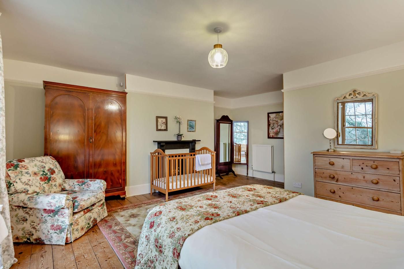 Une chambre à coucher avec une armoire en bois, un canapé à motifs floraux, un berceau, une commode et un lit.