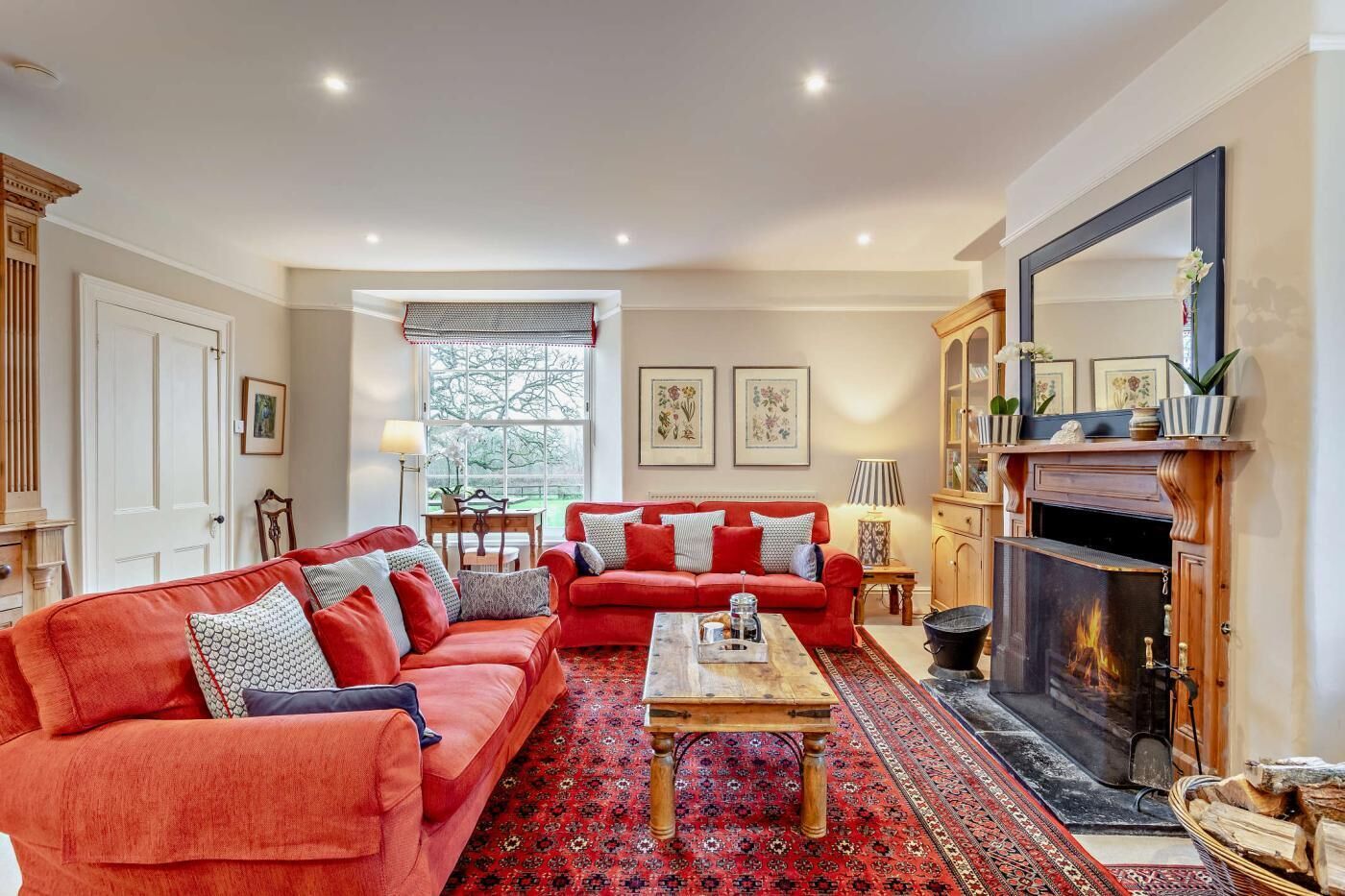 A living room with two red sofas, a coffee table, a fireplace, and a large mirror.