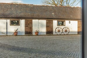 Un bâtiment doté de deux portes et fenêtres en bois, d’une allée gravillonnée et de deux grandes roues fixées au mur.