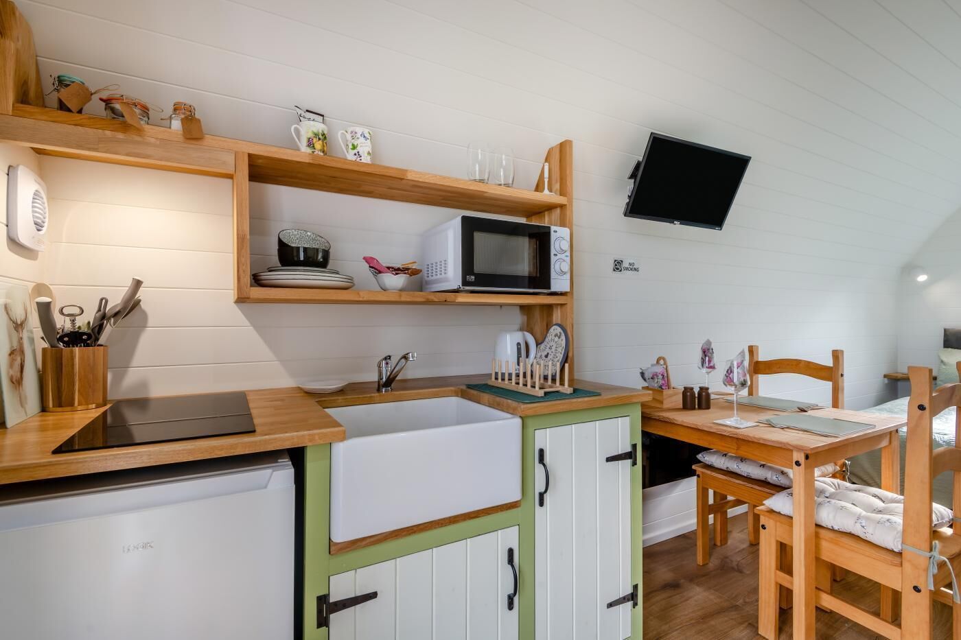 A compact kitchen with a microwave, sink, and wooden shelves.