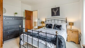 A bedroom with a bed, a dresser, a nightstand, a lamp, a wall art of a deer head, and a wooden door. - 4 Bed in Sheringham (oc-b34006) (Sheringham)