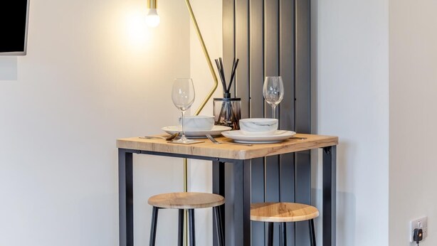 Ein Essbereich mit Tisch für zwei Personen, ausgestattet mit einer modernen Lampe, zwei Weingläsern, einer Schale und einem Teller.