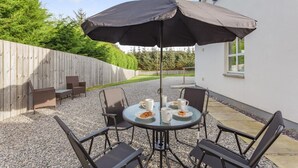 Eine Terrasse mit einem runden Tisch, vier Stühlen und einem großen Sonnenschirm.