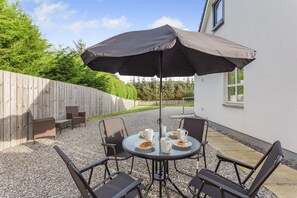 Een terras met een ronde tafel, vier stoelen en een grote parasol.